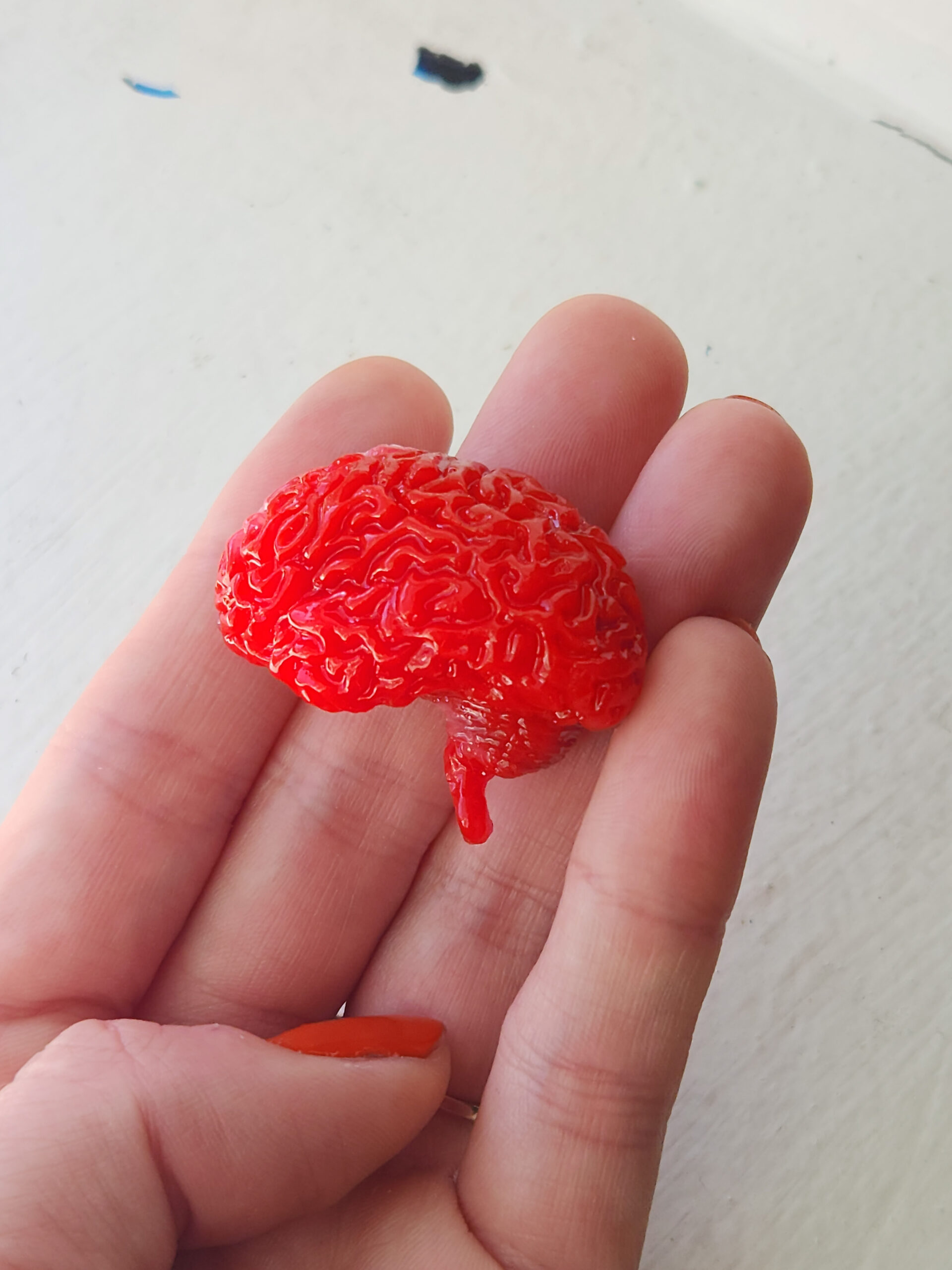 Glossy bright red opaque brain magnet held in natural light.