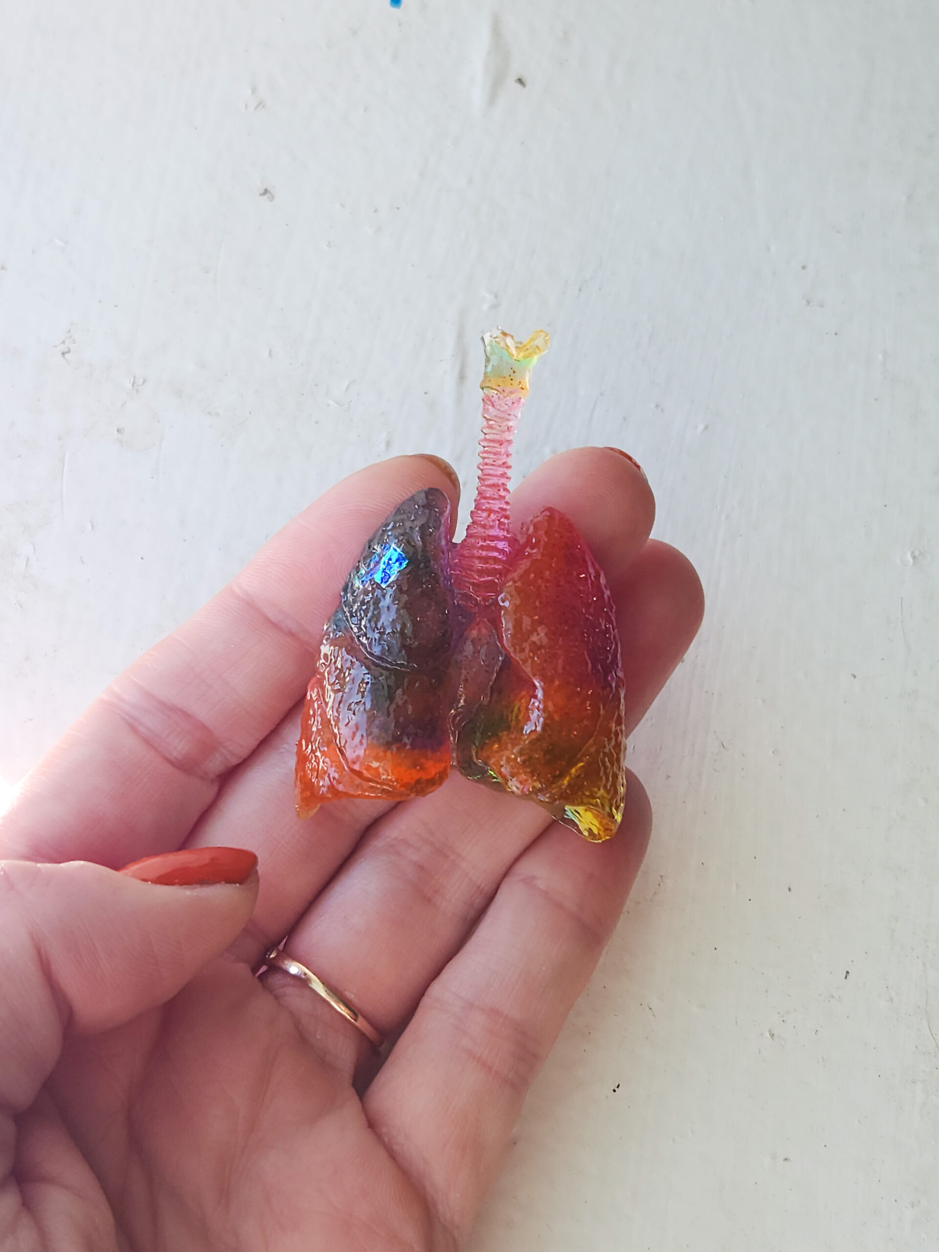 3D human lungs held in natural light, showing yellow, pink, and blue hue with holographic flecks.