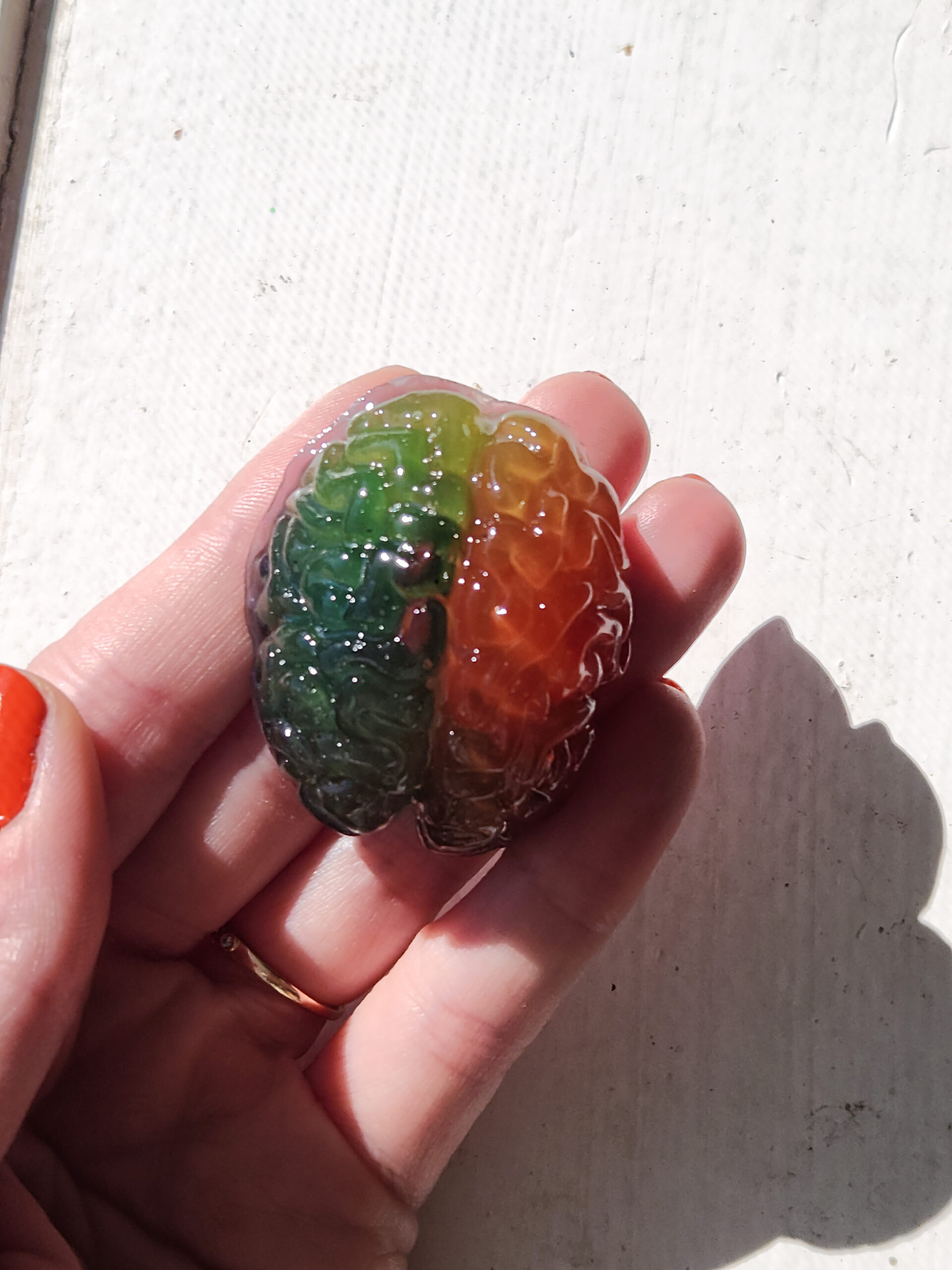 3D resin brain magnet being held out in the sunlight highlighting it's glossy rainbow color