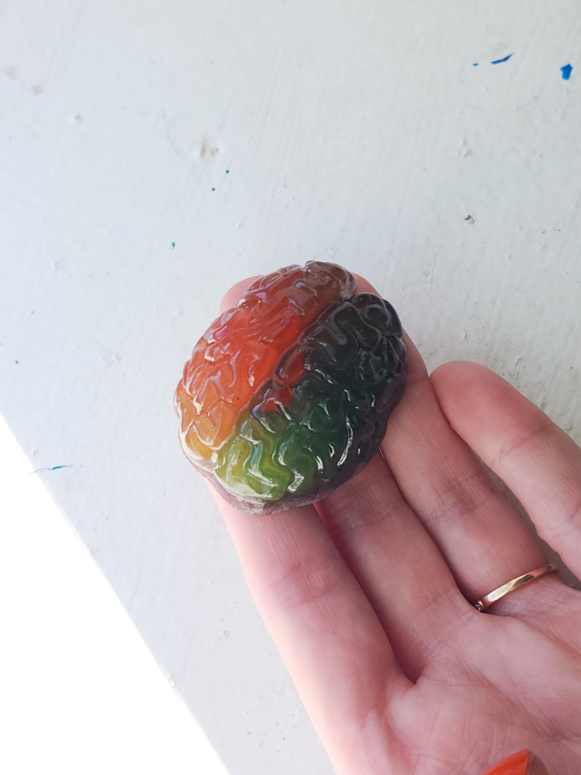 3D resin brain magnet being held out in the sunlight highlighting it's glossy rainbow color