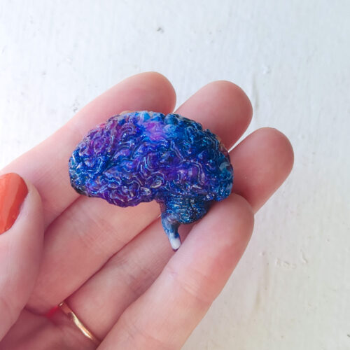 3D resin brain with a glossy sheen held out in the sun. Brain is bright royal blue with swirls of purple and glitter